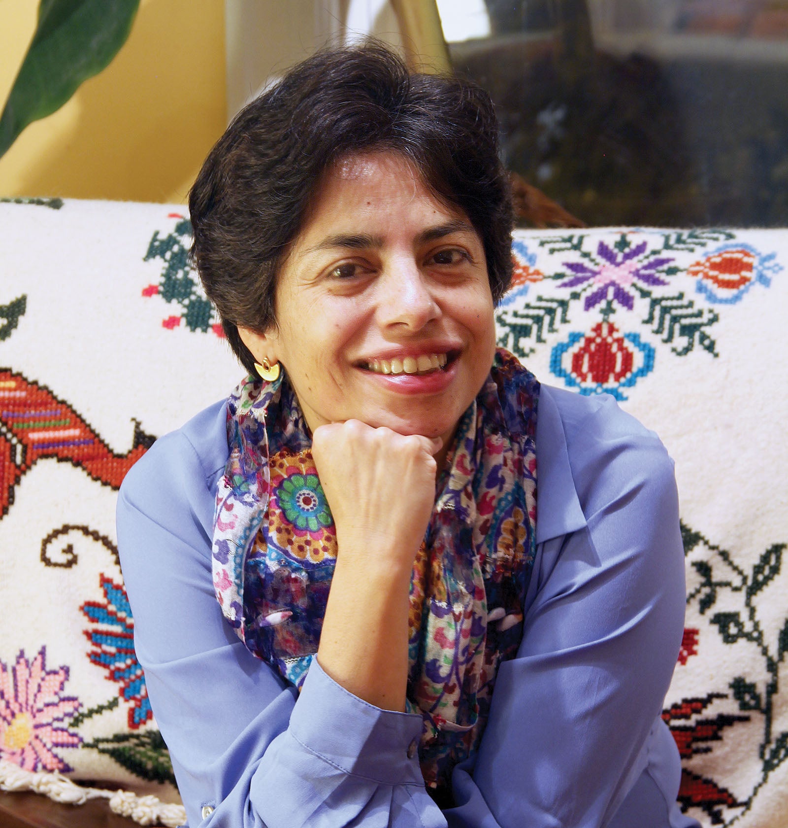 A portrait of Pineda Franco smiling on a couch with a decorative sewn blanket behind her