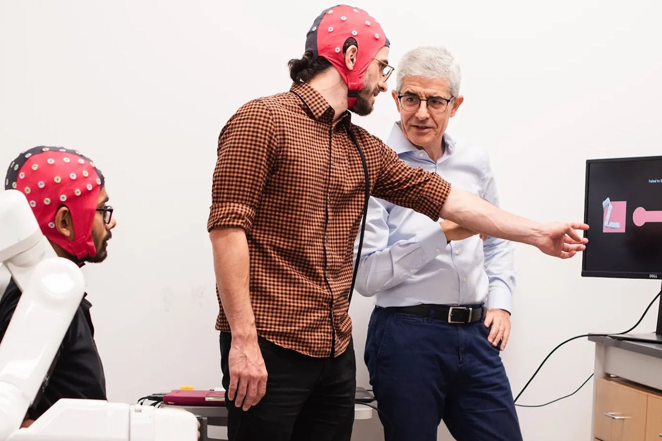 A researcher stands with two people wearing brain research devices.