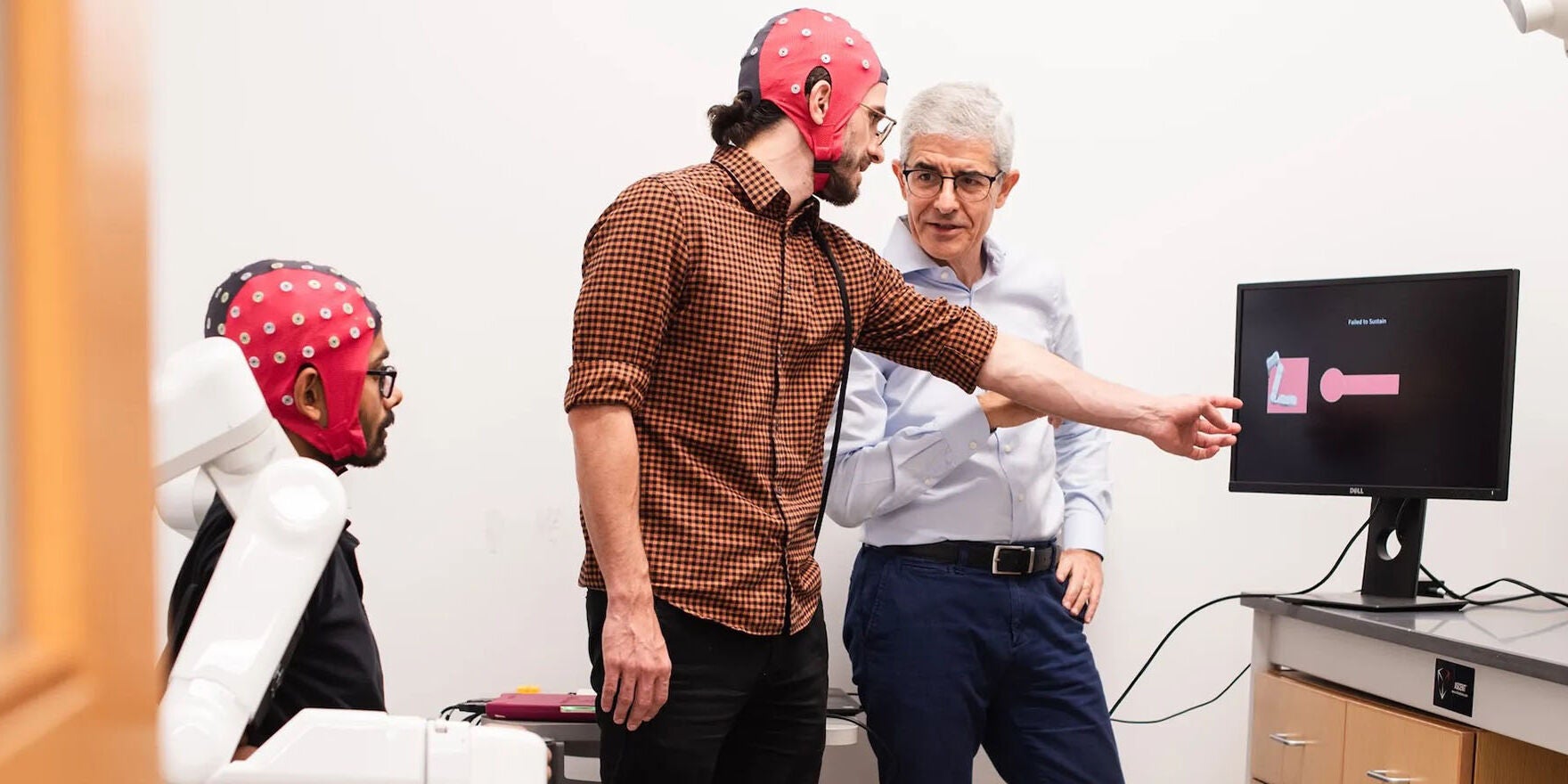 A researcher stands with two people wearing brain research devices.