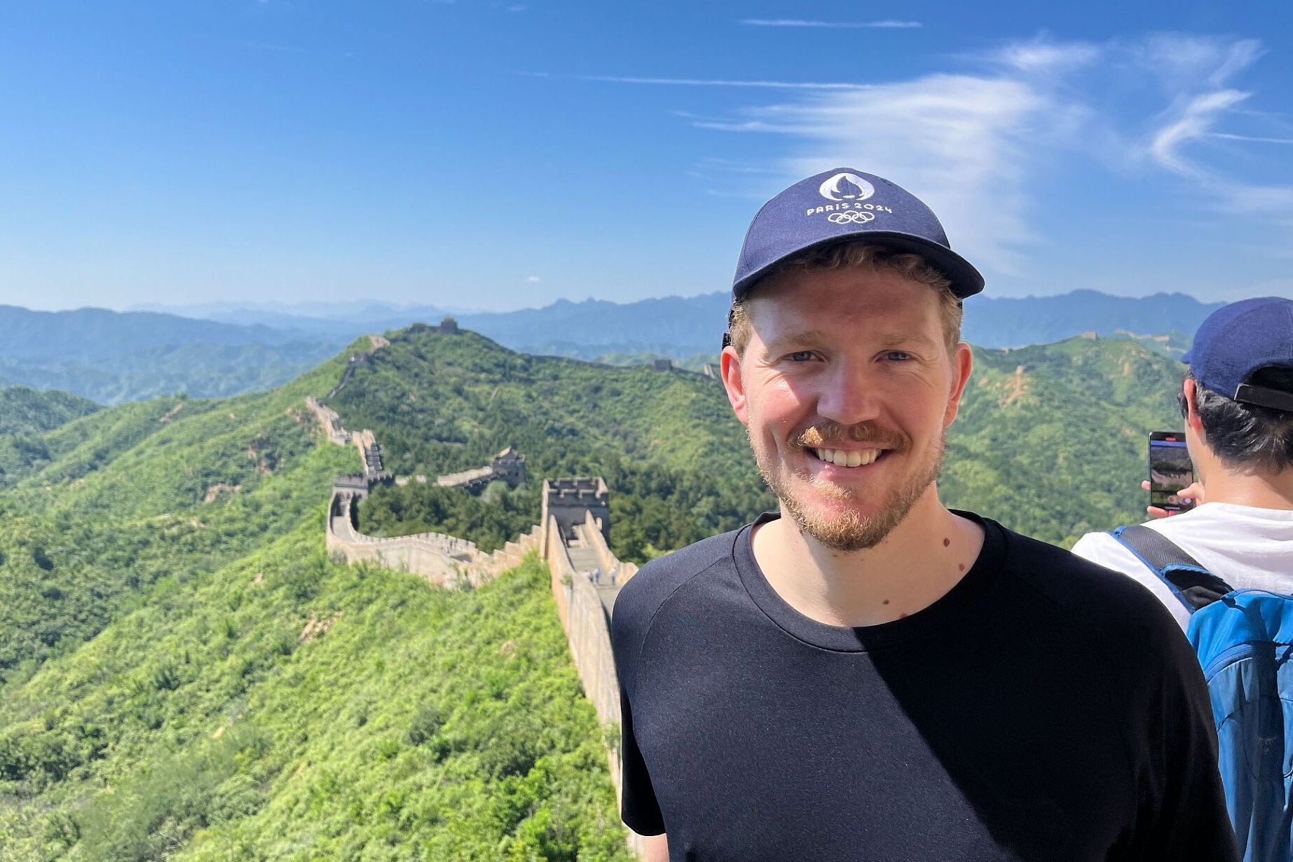 Sebastian DeBeurs smiles while standing atop the Great Wall of China on a beautiful blue sky day