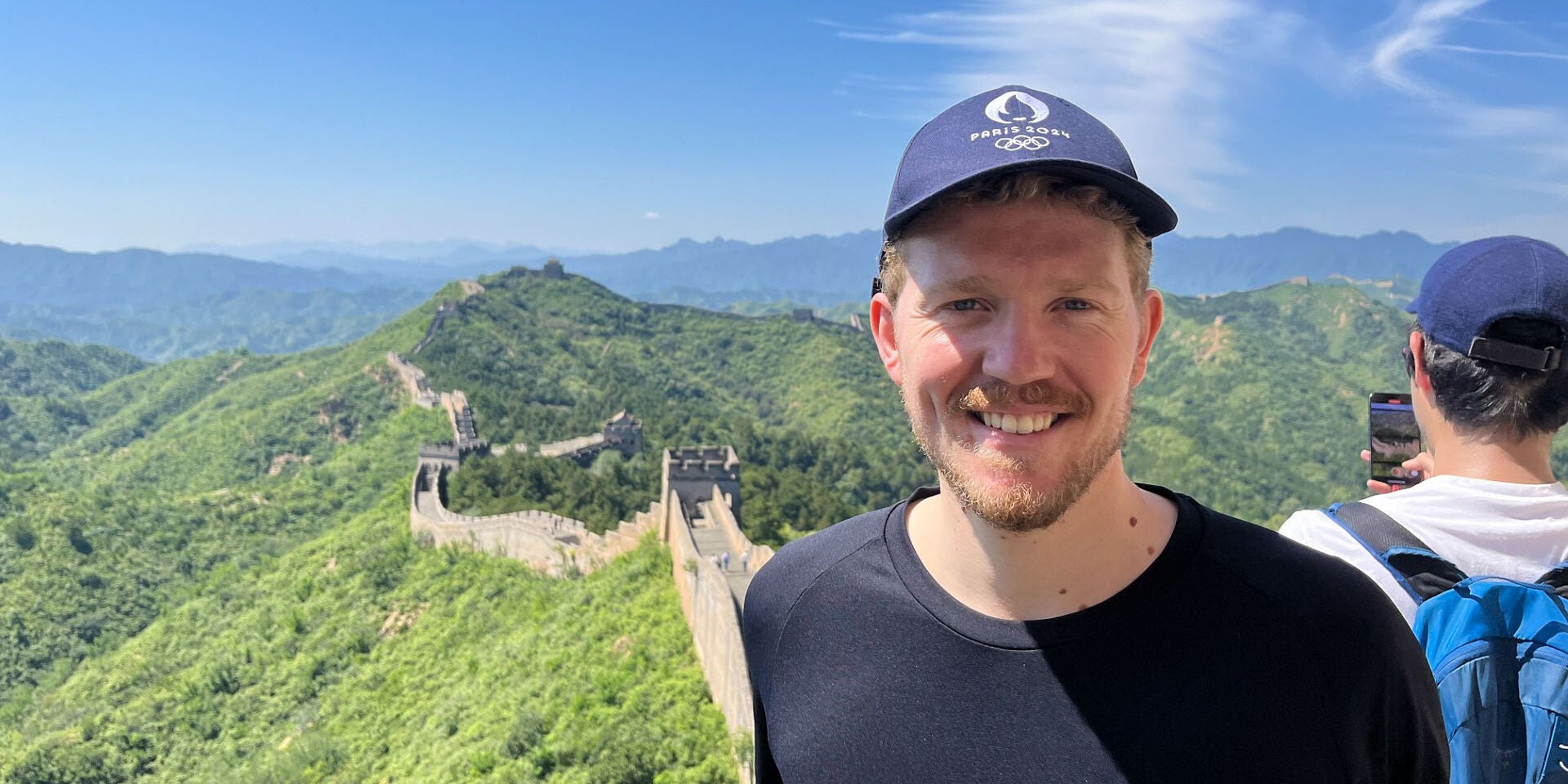 Sebastian DeBeurs smiles while standing atop the Great Wall of China on a beautiful blue sky day